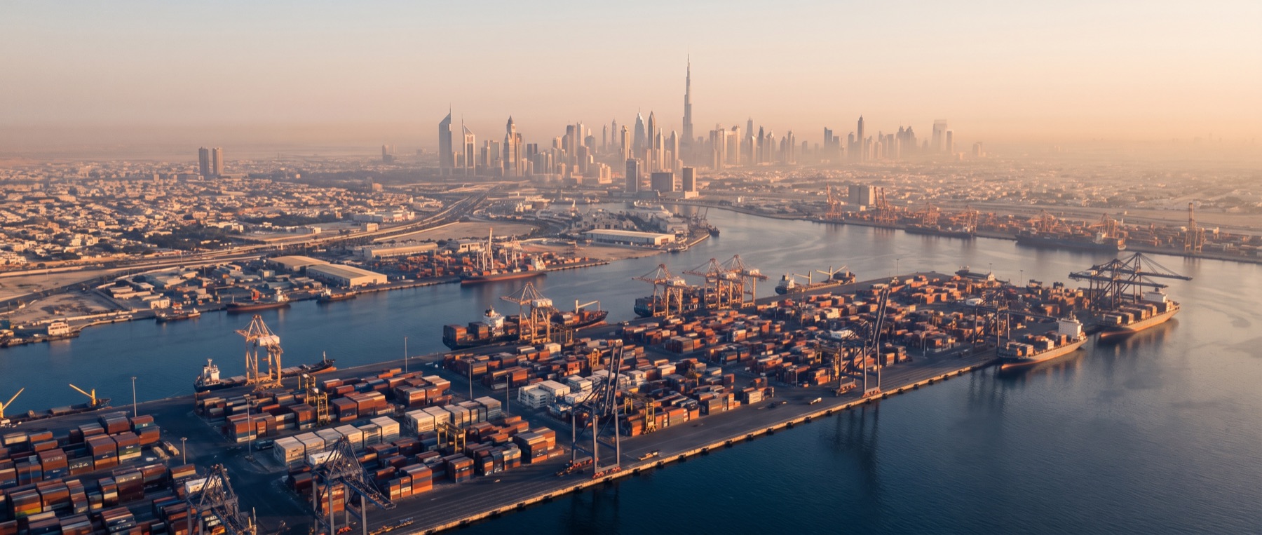 Aerial view of Dubai at golden hour, the skyline behind the working port